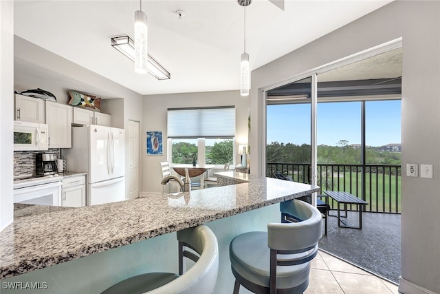 kitchen featuring decorative light fixtures, white cabinetry, white appliances, light tile patterned flooring, and a breakfast bar