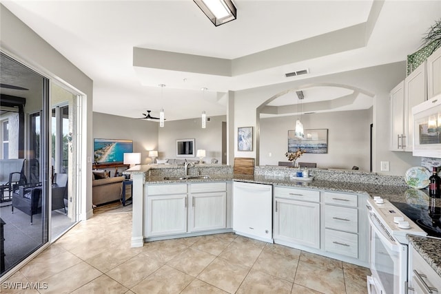 kitchen featuring white appliances, a raised ceiling, kitchen peninsula, pendant lighting, and white cabinetry