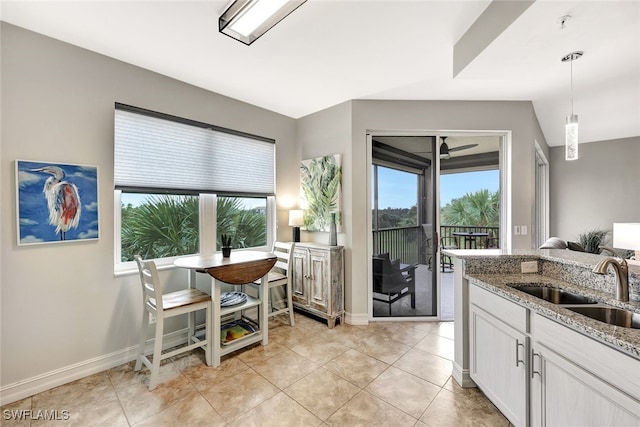 kitchen featuring sink, white cabinets, light tile patterned floors, light stone countertops, and pendant lighting