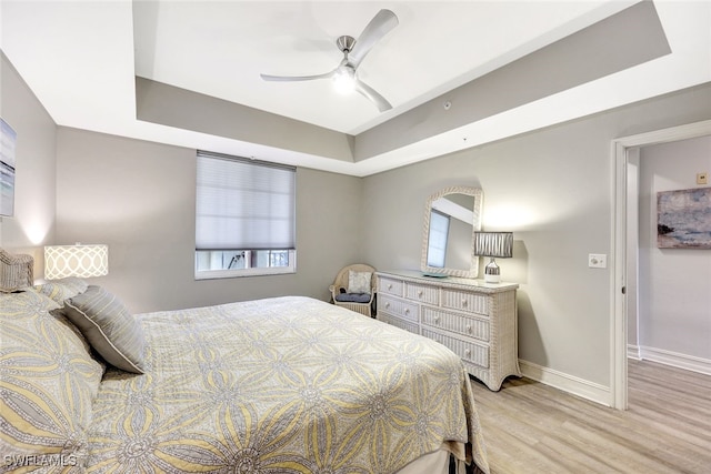 bedroom with ceiling fan, light hardwood / wood-style floors, and a raised ceiling