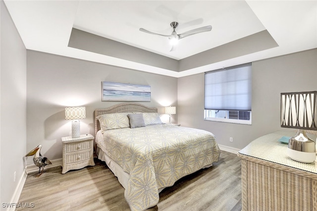 bedroom with hardwood / wood-style flooring, a raised ceiling, and ceiling fan