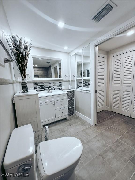 bathroom with a closet, visible vents, toilet, vanity, and baseboards