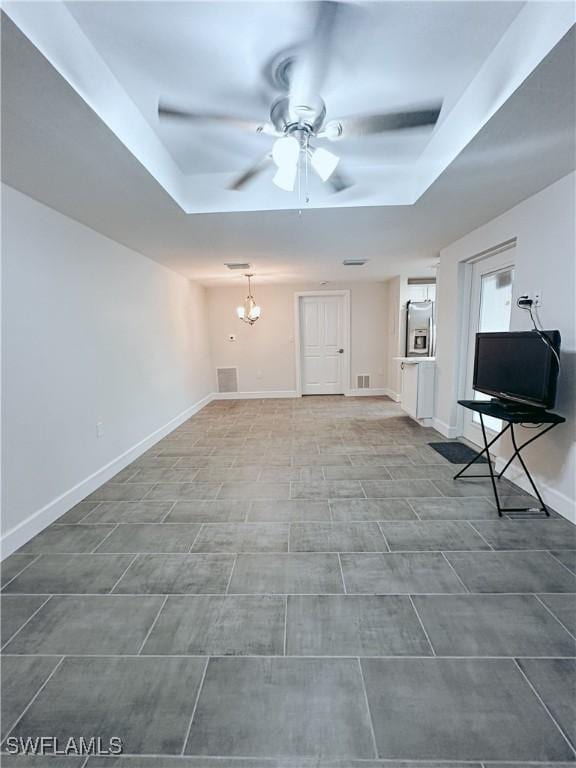 unfurnished living room featuring ceiling fan with notable chandelier, a raised ceiling, visible vents, and baseboards