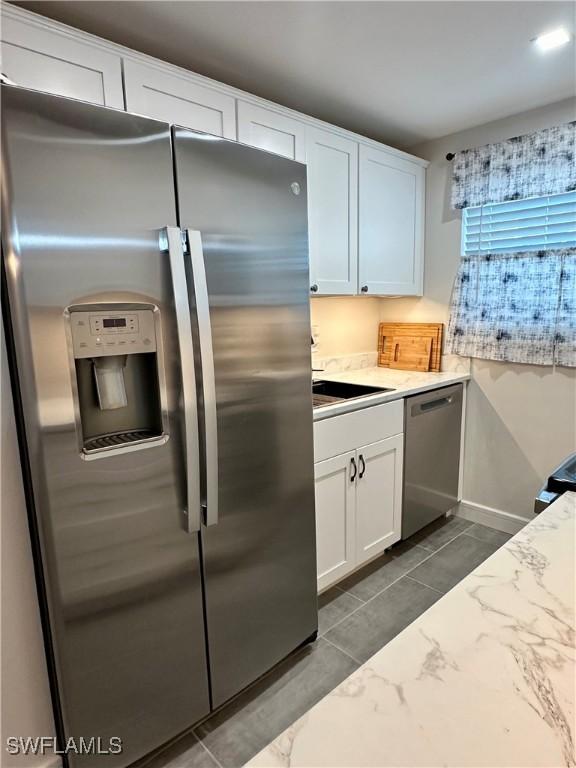 kitchen with appliances with stainless steel finishes, white cabinets, a sink, and light stone counters