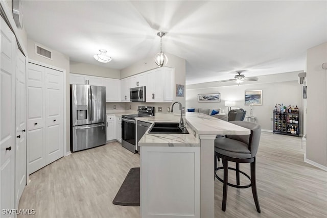 kitchen featuring pendant lighting, kitchen peninsula, sink, white cabinetry, and stainless steel appliances