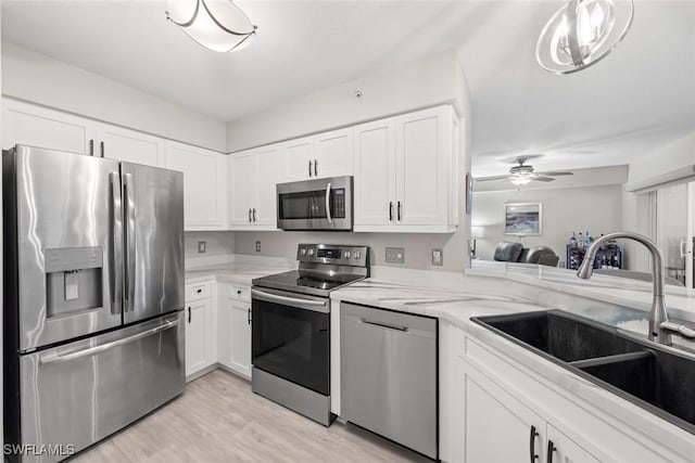 15495 Cedarwood Ln Unit 103, Naples, FL 34110 - kitchen with stainless steel appliances, a sink, white cabinets, light wood-style flooring, and a ceiling fan
