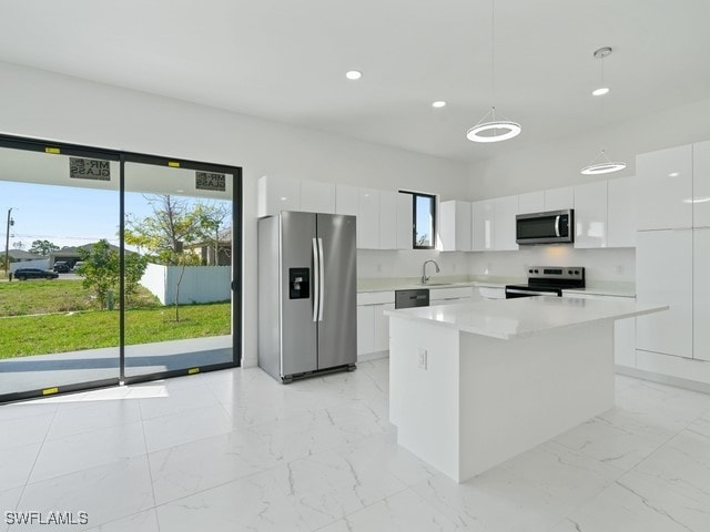 kitchen with appliances with stainless steel finishes, sink, a center island, white cabinets, and hanging light fixtures