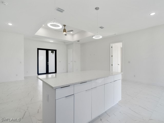 kitchen featuring french doors, a kitchen island, a raised ceiling, white cabinets, and pendant lighting