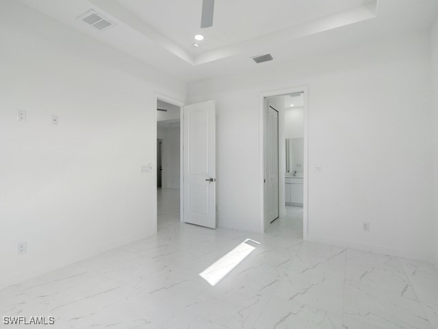 unfurnished bedroom featuring connected bathroom, ceiling fan, and a tray ceiling