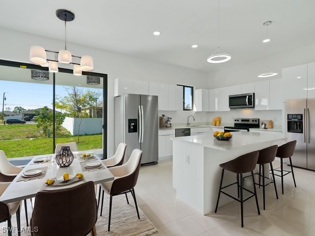 kitchen featuring white cabinetry, decorative light fixtures, a kitchen island, sink, and appliances with stainless steel finishes