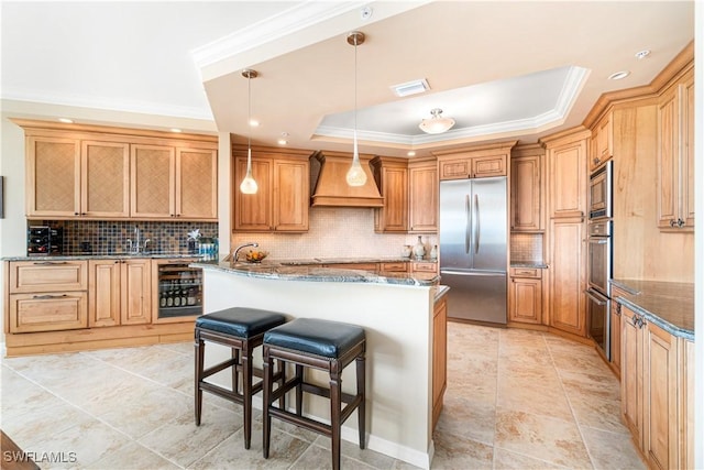 kitchen featuring a raised ceiling, decorative light fixtures, dark stone counters, built in appliances, and a center island