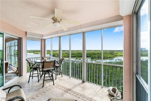 sunroom with ceiling fan and a water view