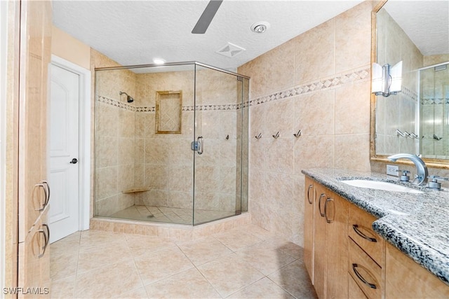 bathroom with walk in shower, vanity, tile walls, tile patterned floors, and a textured ceiling