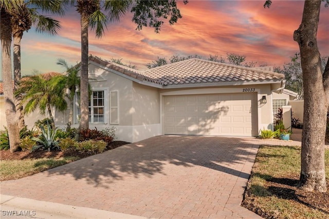 mediterranean / spanish-style home featuring a garage, decorative driveway, a tile roof, and stucco siding