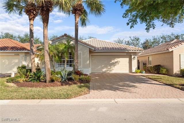 mediterranean / spanish-style home featuring a garage, decorative driveway, a tile roof, and stucco siding