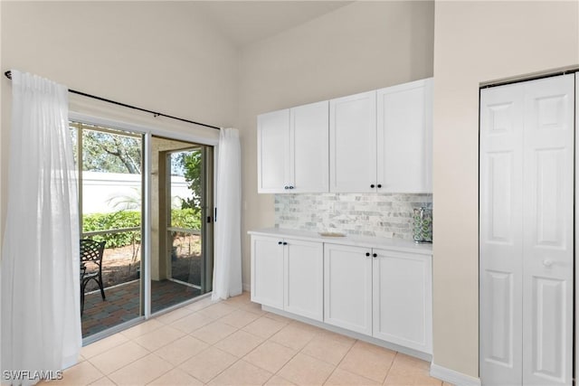 interior space with light tile patterned floors, white cabinets, a high ceiling, and tasteful backsplash