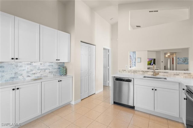 kitchen with sink, white cabinets, light tile patterned flooring, stainless steel dishwasher, and a high ceiling