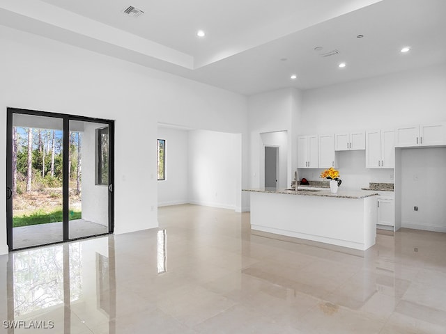 kitchen with sink, white cabinetry, a kitchen island with sink, and light stone counters