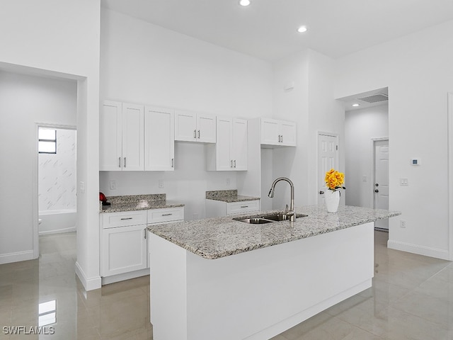 kitchen with light stone countertops, a kitchen island with sink, white cabinetry, and sink