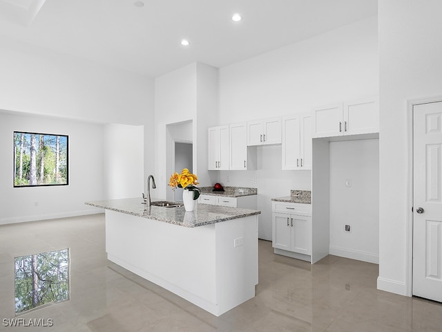 kitchen with sink, white cabinetry, light stone counters, a high ceiling, and a kitchen island with sink