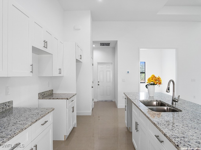 kitchen featuring light stone counters, white cabinets, and sink