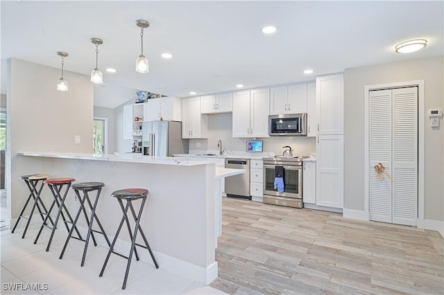 kitchen with kitchen peninsula, hanging light fixtures, white cabinetry, a kitchen bar, and stainless steel appliances