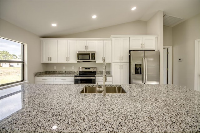 kitchen featuring vaulted ceiling, appliances with stainless steel finishes, white cabinets, and light stone counters