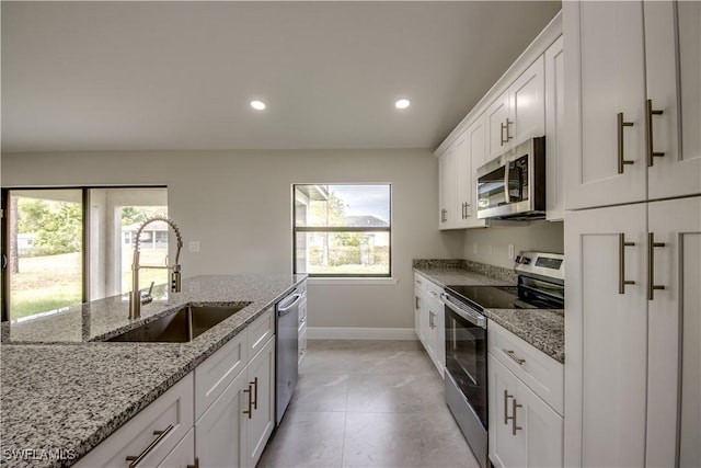 kitchen featuring sink, light tile patterned floors, appliances with stainless steel finishes, white cabinets, and light stone counters