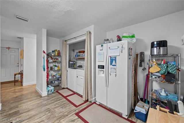 kitchen with white fridge with ice dispenser, separate washer and dryer, a textured ceiling, and light hardwood / wood-style flooring