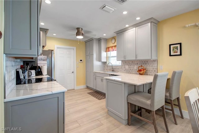 kitchen featuring backsplash, kitchen peninsula, sink, light hardwood / wood-style flooring, and gray cabinetry