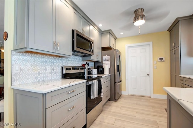 kitchen featuring ceiling fan, stainless steel appliances, gray cabinetry, tasteful backsplash, and light hardwood / wood-style flooring