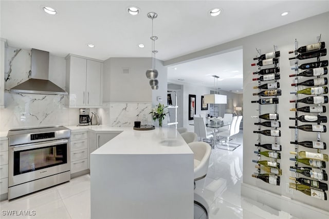 kitchen featuring a breakfast bar area, decorative backsplash, hanging light fixtures, wall chimney range hood, and stainless steel electric range