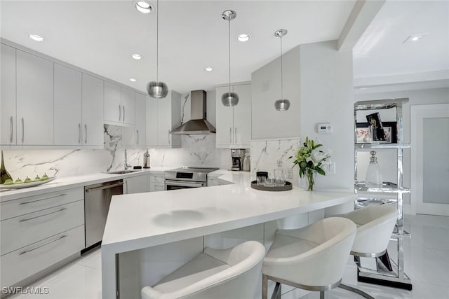 kitchen featuring a breakfast bar area, pendant lighting, stainless steel appliances, decorative backsplash, and wall chimney range hood