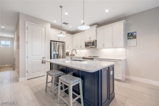 kitchen featuring appliances with stainless steel finishes, white cabinetry, an island with sink, sink, and hanging light fixtures