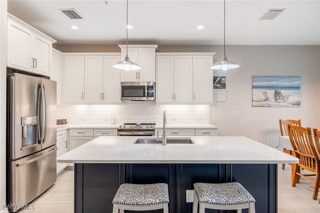 kitchen with a center island with sink, stainless steel appliances, tasteful backsplash, hanging light fixtures, and sink