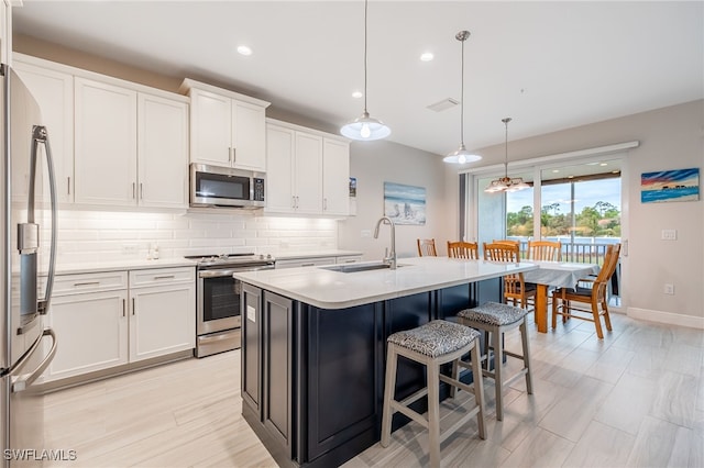 kitchen with hanging light fixtures, white cabinets, a kitchen island with sink, and appliances with stainless steel finishes