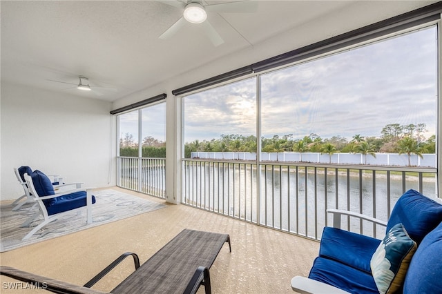 sunroom with ceiling fan and a water view