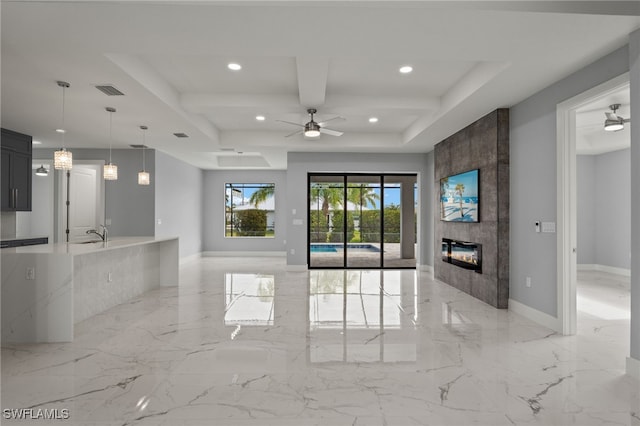 unfurnished living room with sink, a tile fireplace, beam ceiling, and ceiling fan