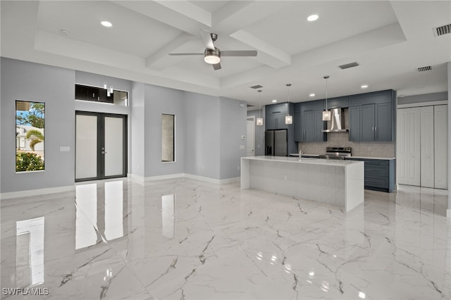 kitchen featuring decorative light fixtures, wall chimney range hood, stainless steel appliances, french doors, and an island with sink