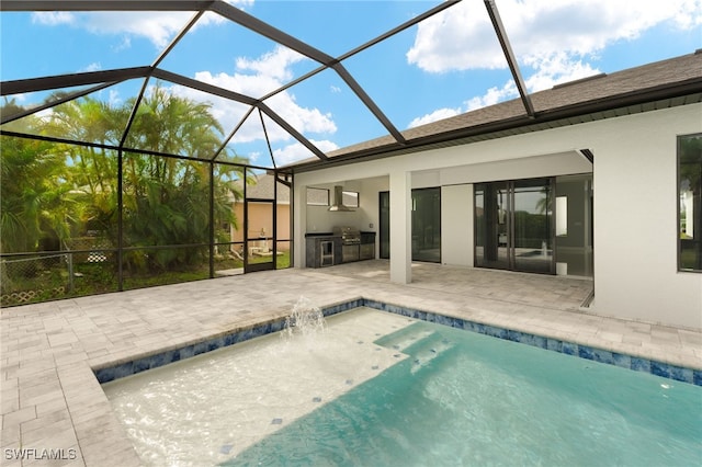 view of pool featuring glass enclosure, an outdoor kitchen, pool water feature, and a patio area