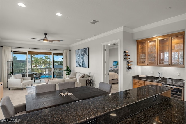 kitchen with sink, a kitchen breakfast bar, wine cooler, ornamental molding, and dark stone counters