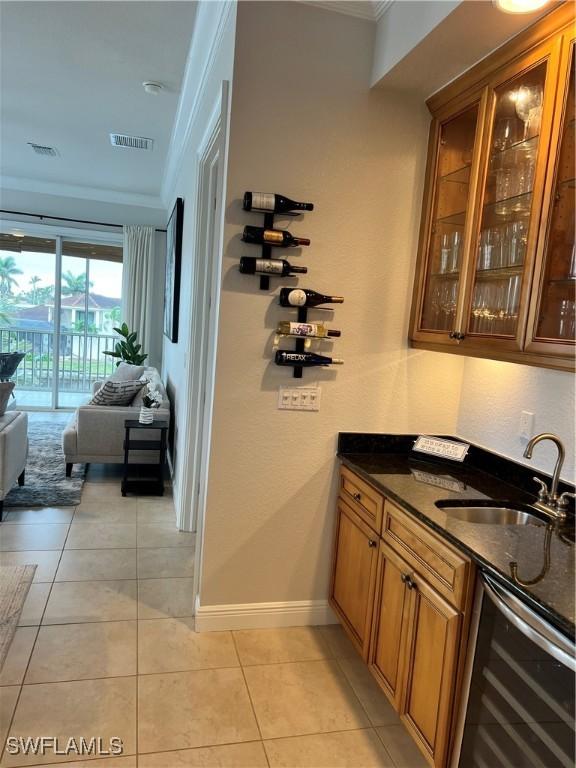 bar featuring sink, wine cooler, dark stone counters, ornamental molding, and light tile patterned floors