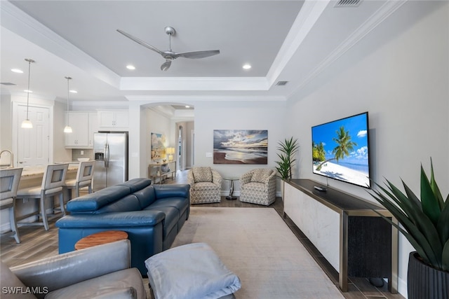 living room featuring ceiling fan, dark hardwood / wood-style flooring, ornamental molding, and a tray ceiling