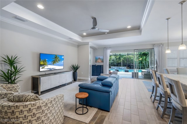 living room featuring a raised ceiling, ceiling fan, and ornamental molding