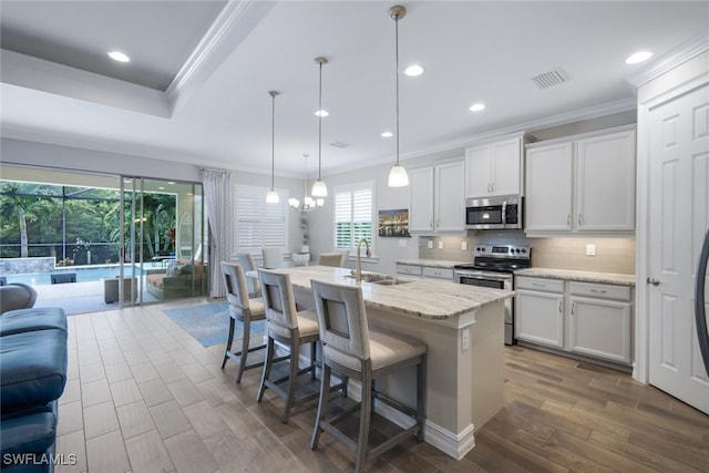 kitchen with appliances with stainless steel finishes, an island with sink, white cabinets, decorative light fixtures, and sink