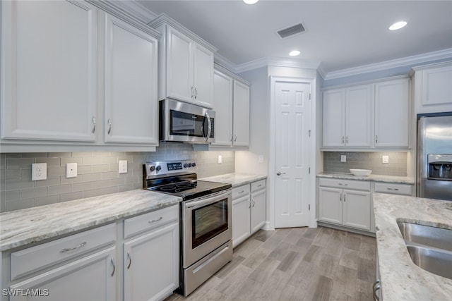 kitchen featuring stainless steel appliances, crown molding, light stone countertops, decorative backsplash, and white cabinetry