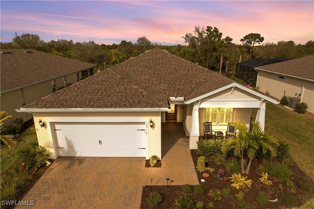 ranch-style house with decorative driveway, roof with shingles, a porch, an attached garage, and cooling unit