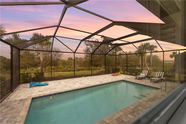 pool at dusk featuring a lanai and a patio