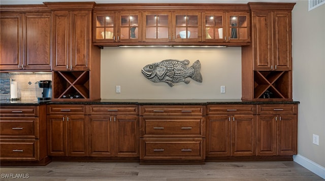 bar with dark stone counters, light hardwood / wood-style floors, and backsplash