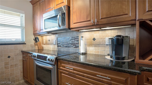 kitchen featuring stainless steel appliances, dark stone counters, and backsplash